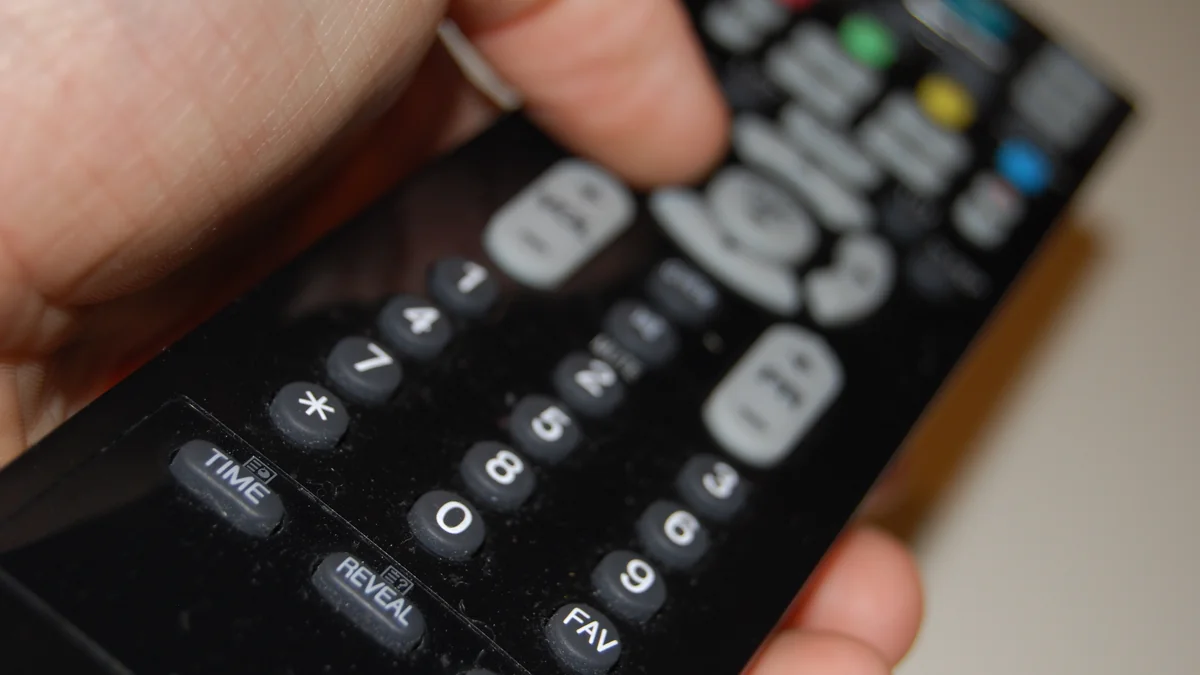 Close-up of a hand pressing buttons on a television remote control while channel surfing