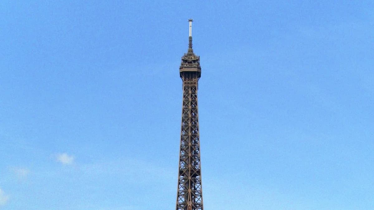 The upper section of the Eiffel Tower in Paris, France, set against a clear blue sky