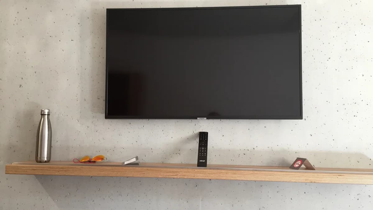 Wall-mounted Samsung television with its screen off and a remote control resting on a shelf below it
